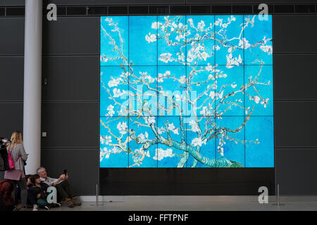 Visitors sit in front of a giant screen featuring Almond Blossom by Vincent Van Gogh at the Van Gogh museum in Amsteram Stock Photo