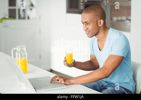 Smiling man using laptop and drinking orange juice Stock Photo
