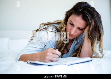 woman lying in her bed writing in a book Stock Photo