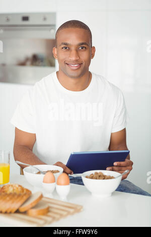 Young man using tablet and eating breakfast in kitchen Stock Photo