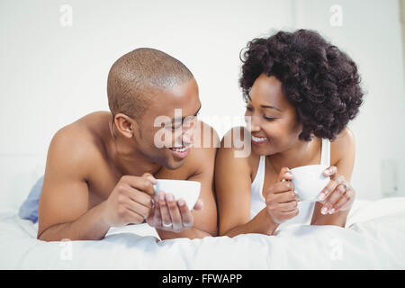 Happy couple lying on bed while holding cups Stock Photo