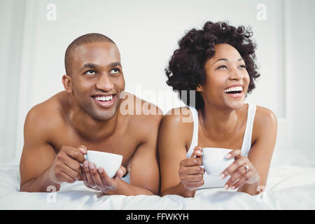 Happy couple lying on bed while holding cups Stock Photo