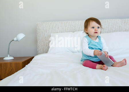 Adorable toddler sitting on bed bitting duck toy at bedroom Stock Photo ...