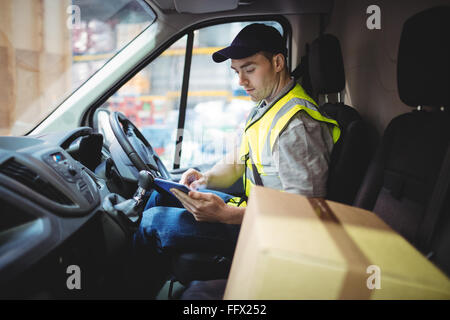 Delivery driver using tablet in van with parcels on seat Stock Photo