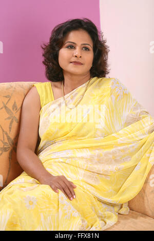South Asian Indian young lady wearing yellow sari sitting on sofa MR#687N Stock Photo