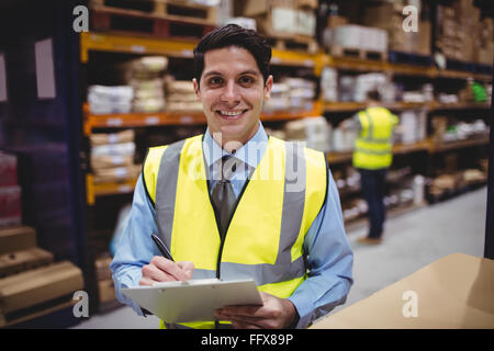 Smiling warehouse manager writing on clipboard Stock Photo