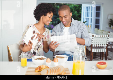 Smiling couple reading magazine and documents during breakfast Stock Photo