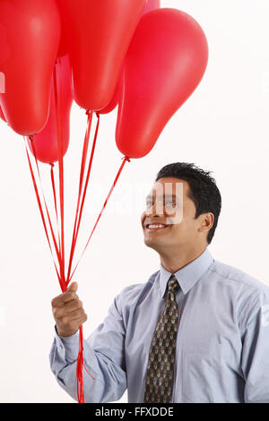 Businessman looking at red color gas balloons holding in one hand MR#703T Stock Photo