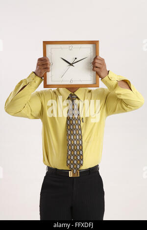 Businessman holding wall clock in both hands over his face and hiding it MR#703T Stock Photo