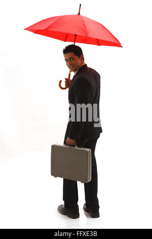 Businessman holding red opened umbrella on head with briefcase in other hand MR#703T Stock Photo
