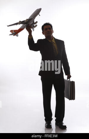 Businessman in silhouette holding passenger aeroplane in flying angle in one hand and briefcase in other hand MR#703T,NO PR Stock Photo