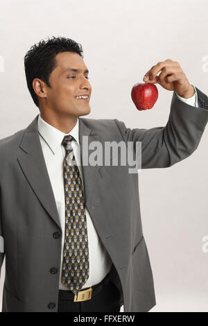 Businessman holding red apple in index finger with thumb of right hand MR#703T Stock Photo