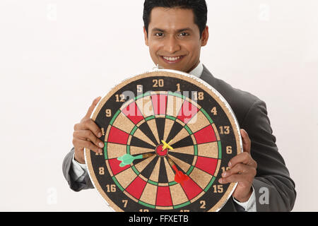 Businessman holding dart board in front of his chest showing three darts on centre  in both hands MR#703T Stock Photo