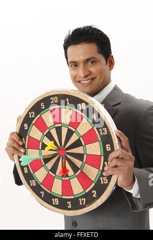 Businessman holding dart board in front of his chest showing three darts on centre in both hands MR#703T Stock Photo