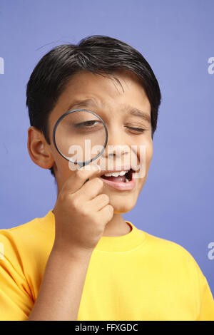 Ten year old boy looking through magnifying glass and other eye closed MR#703V Stock Photo