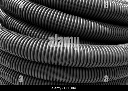 Flexible, black, one above the other lying plastic pipes in sunlight. Taken in close-up. Stock Photo