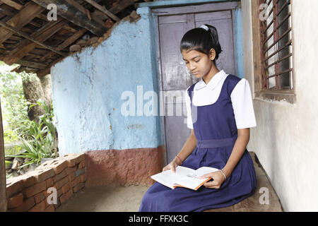 School going girl sitting on bench in veranda of old rural house and reading text book , Maharashtra , India MR#703Z Stock Photo