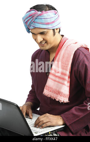 Rich Indian farmer tied gamcha on head another kept on shoulder operating laptop MR#743A Stock Photo
