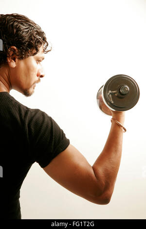 South Asian Indian man wearing black T shirt and curly oily hair building arms muscles with steel dumbbell MR#686H Stock Photo