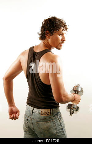 South Asian Indian man wearing black vest and curly oily hair building arms muscles with steel dumbbell MR#686H Stock Photo