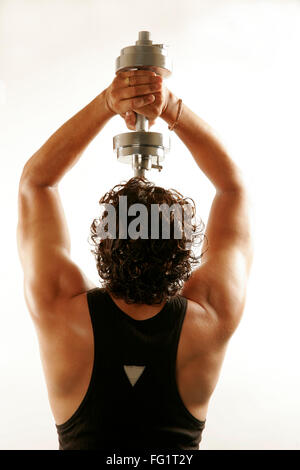 South Asian Indian man wearing black vest and curly oily hair building arms muscles with steel dumbbell MR#686H Stock Photo