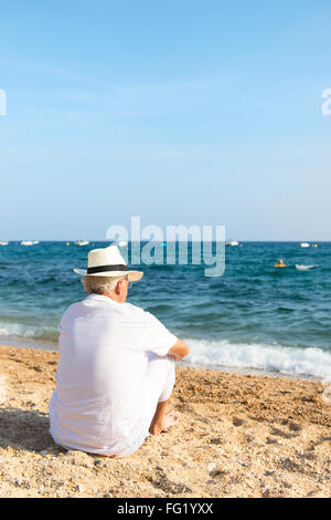 Senior man in white suit sitting at the beach Stock Photo