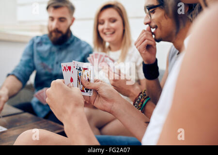 Group of friends sitting together playing cards. Focus on playing cards in hands of a woman during a party. Stock Photo