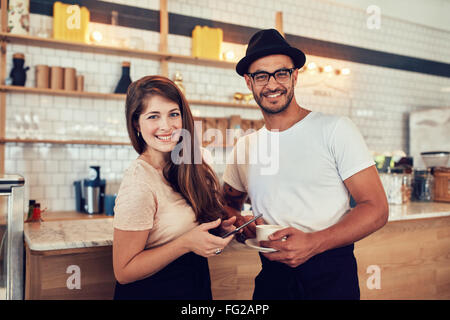 Portrait of happy young couple at cafe with a cup of coffee and digital tablet. Caucasian couple standing together a cafe counte Stock Photo