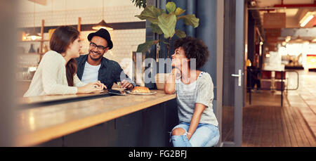 Portrait of three young people sitting together at a cafe. Group of young friends meeting in a coffee shop. Stock Photo