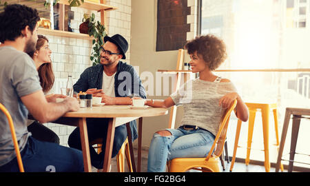 Portrait of a young group of friends meeting in a cafe. Young men and women sitting at cafe table and talking. Stock Photo