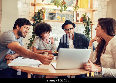 Portrait of young people sitting around a table in cafe with a laptop. Creative team discussing new business project at a coffee Stock Photo