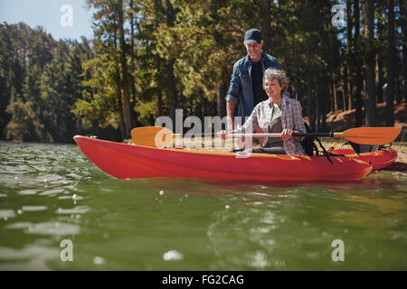 Portrait of mature man giving instruction to woman paddling a kayak in the lake. Senior woman getting kayaking lessons from a ma Stock Photo