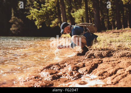 Portrait of mature man washing his face with lake water. Senior caucasian man washing face from lake water on a summer day. Stock Photo
