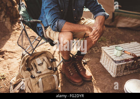 Close up shot of mature man sitting on a chair. Man relaxing at campsite, focus on hands. Stock Photo