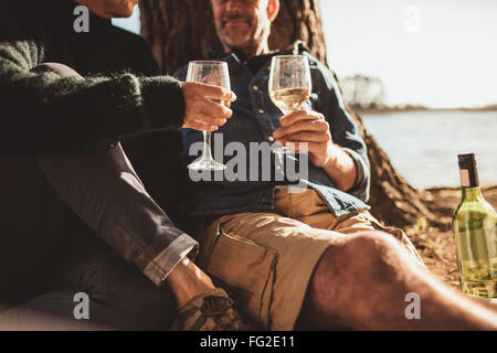 Cropped image of loving mature couple sitting together with a glass of wine. Man and woman camping and holding a glass of wine. Stock Photo