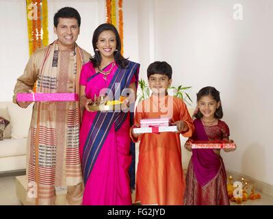 Mother holding pooja thali with family holding gift boxes standing in house MR#702R,MR#702S,MR#702T,MR#702U Stock Photo