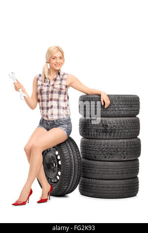 Vertical shot of a female mechanic holding a wrench and sitting on a tire isolated on white background Stock Photo