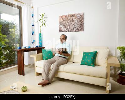 Old man reading magazine sitting on sofa MR#702T Stock Photo