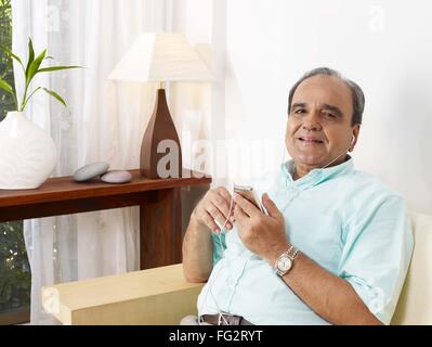 Old man listening to music on headphones sitting on sofa MR#702T Stock Photo