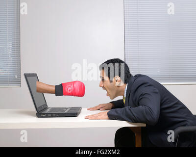 Boxing punch through laptop in front of executive MR#779K Stock Photo