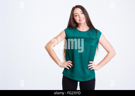 Pretty smiling young woman in green top standing with hands on waist over white background Stock Photo