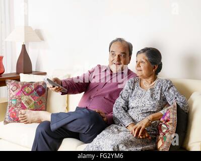 Old couple watching TV using remote control MR#702T,702S Stock Photo