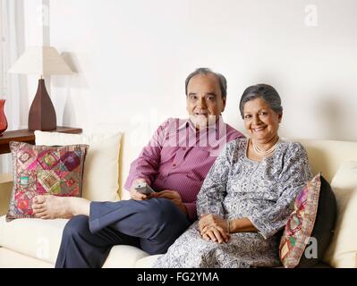 Old couple using remote control sitting on sofa MR#702T,702S Stock Photo