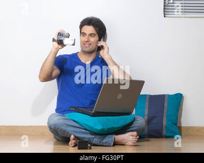 Man talking on mobile holding video camera and laptop on his lap ; MR#779L Stock Photo