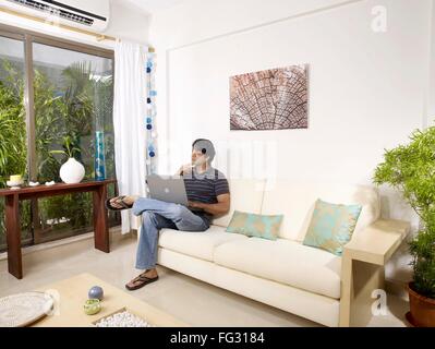 Young man in own thought with laptop sitting on sofa MR#702V Stock Photo