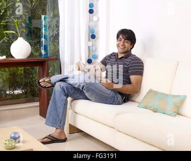Young man holding newspaper sitting on sofa MR#702V Stock Photo