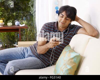 Young man listening to music on headphones sitting on sofa MR#702V Stock Photo
