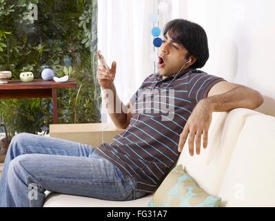 Young man yawning listening to music on headphones sitting on sofa MR#702V Stock Photo