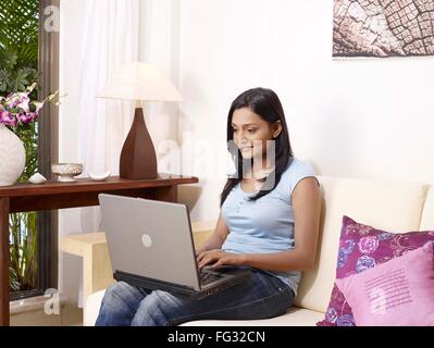 Young lady operating laptop sitting on sofa MR#702U Stock Photo