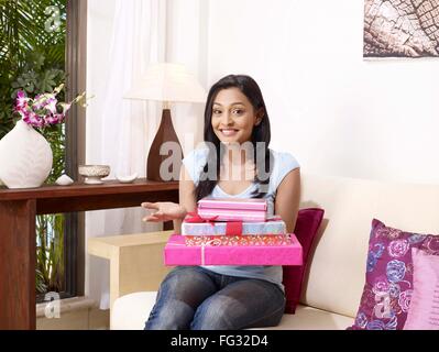 Young lady showing present boxes sitting on sofa MR#702U Stock Photo